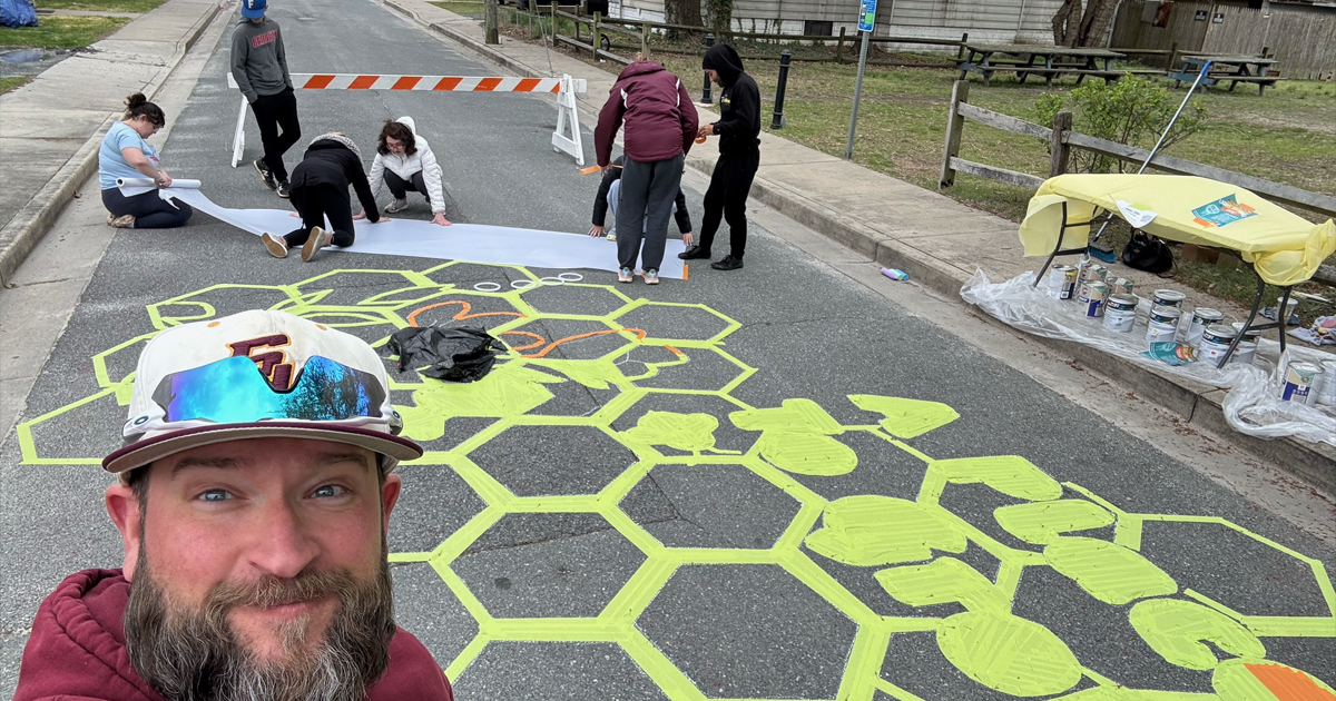 Professor Ryan Weaver standing in front of street mural in progress